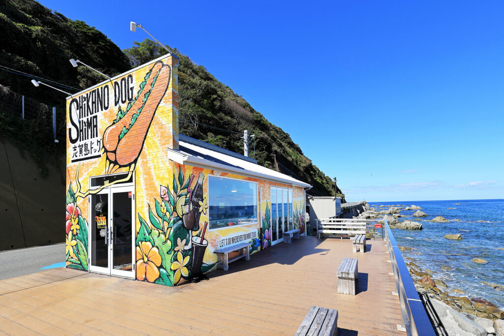福岡市東区志賀島にある「志賀島ドッグ 本店」の外観。海沿いのテラス席と青い海が広がるロケーション